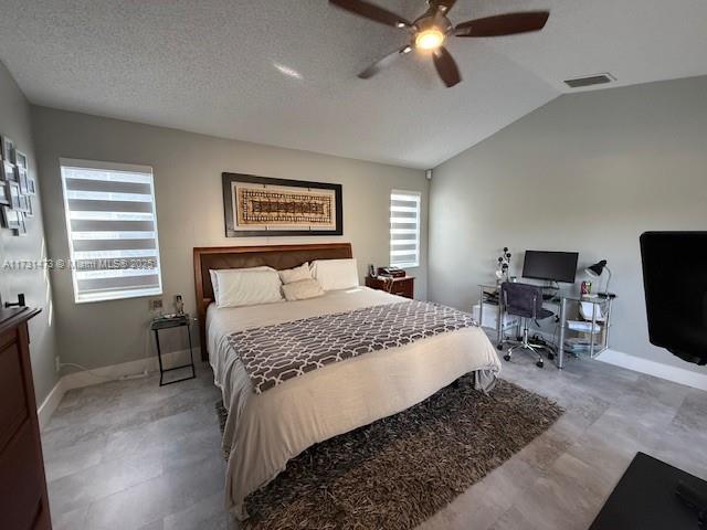 bedroom with vaulted ceiling, a textured ceiling, and ceiling fan