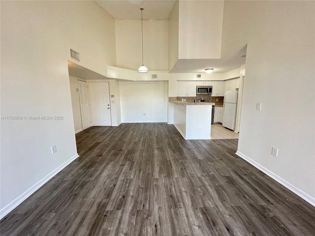 unfurnished living room featuring a towering ceiling and dark hardwood / wood-style floors