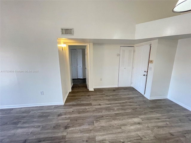 empty room with dark hardwood / wood-style flooring and a high ceiling