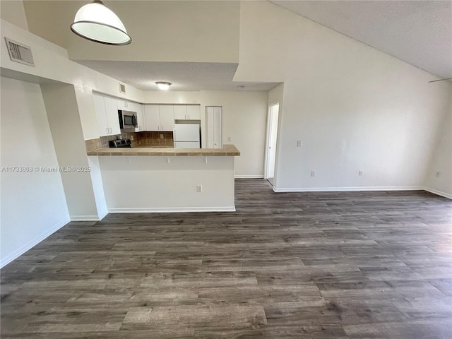 kitchen featuring tasteful backsplash, white cabinets, a kitchen bar, kitchen peninsula, and white fridge