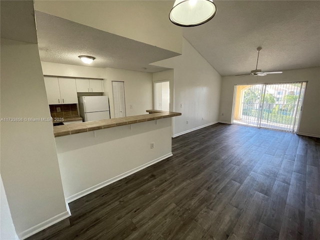 kitchen with tile countertops, white cabinets, white fridge, ceiling fan, and kitchen peninsula