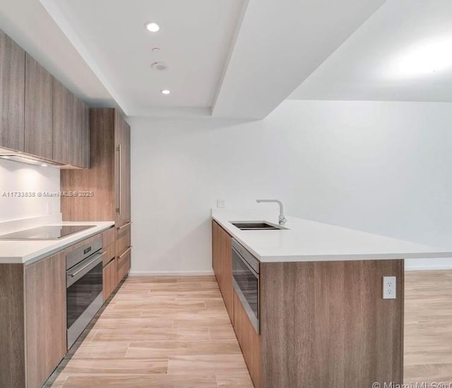 kitchen featuring sink, kitchen peninsula, black electric stovetop, oven, and light hardwood / wood-style floors