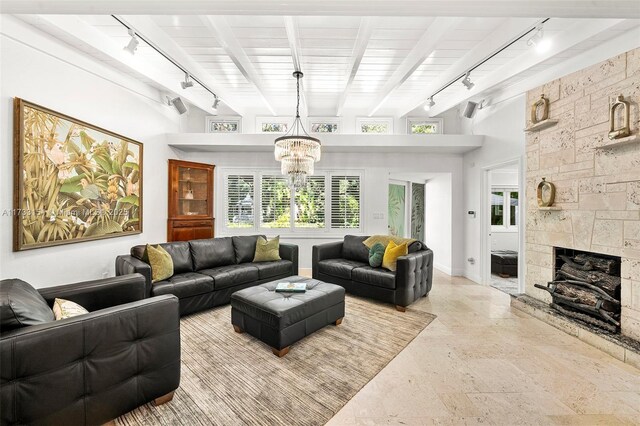 living room featuring beamed ceiling, a stone fireplace, an inviting chandelier, and wooden ceiling