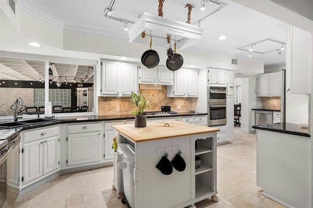 kitchen with white cabinetry, ornamental molding, a center island, and butcher block counters