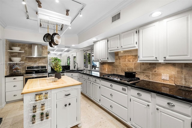 kitchen with crown molding, stainless steel appliances, wall chimney range hood, and white cabinets