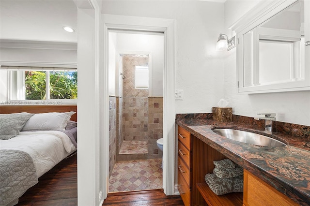 bathroom featuring toilet, crown molding, a tile shower, vanity, and hardwood / wood-style floors