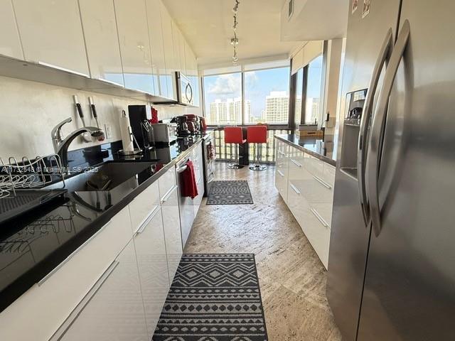 kitchen with a city view, stainless steel appliances, dark countertops, white cabinetry, and a wall of windows