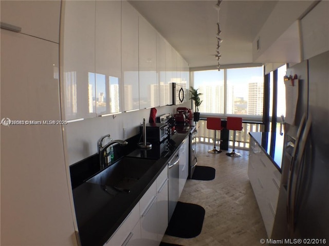 kitchen with dark countertops, appliances with stainless steel finishes, rail lighting, white cabinetry, and a sink