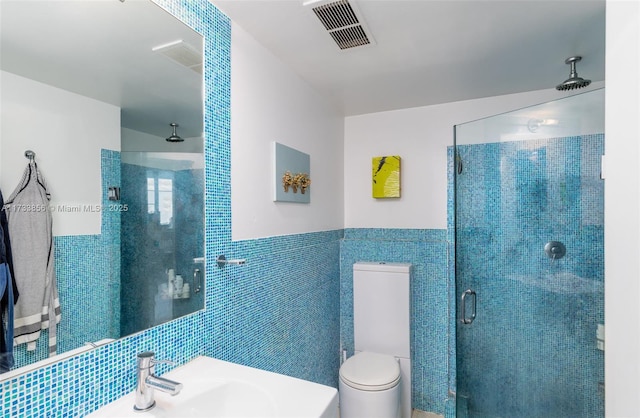 bathroom featuring a shower with door, sink, tile walls, and toilet