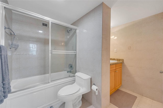 full bathroom with toilet, bath / shower combo with glass door, tile walls, vanity, and tile patterned flooring