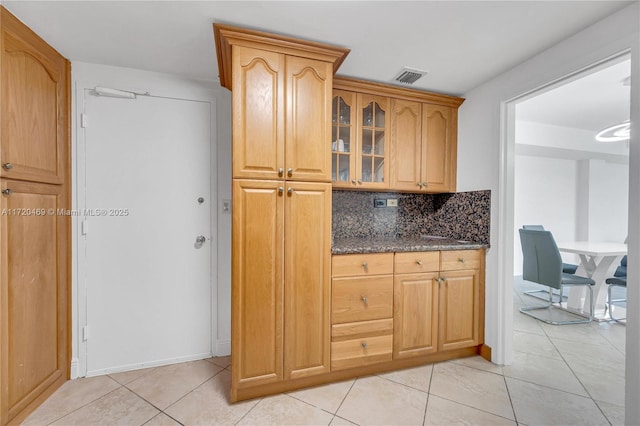 kitchen featuring tasteful backsplash, light tile patterned floors, and dark stone counters