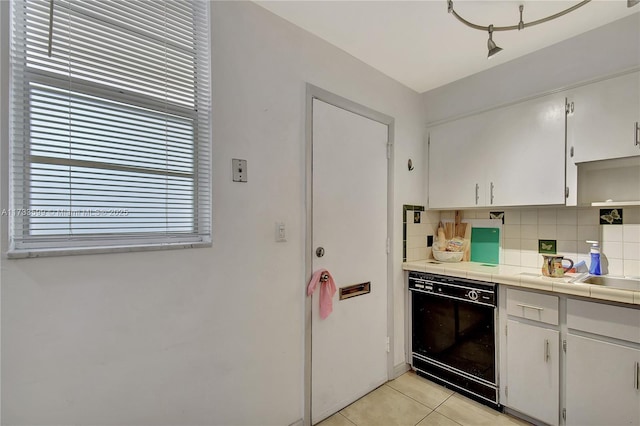 kitchen featuring light tile patterned floors, backsplash, tile counters, black dishwasher, and white cabinets