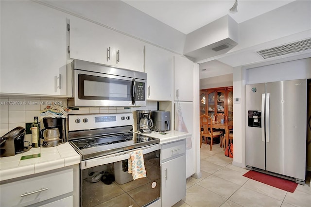 kitchen with light tile patterned flooring, tasteful backsplash, white cabinetry, tile counters, and stainless steel appliances