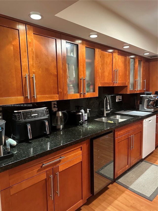 kitchen with sink, dark stone countertops, white dishwasher, wine cooler, and light hardwood / wood-style floors