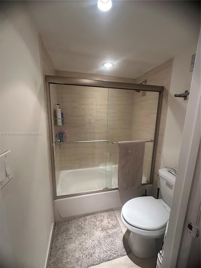 bathroom featuring toilet, bath / shower combo with glass door, and tile patterned flooring