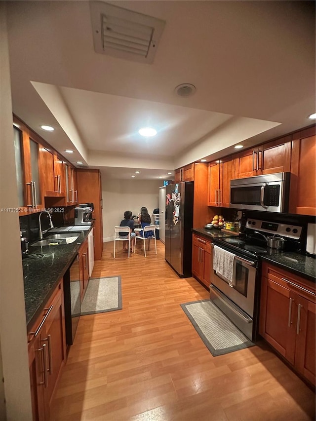 kitchen featuring stainless steel appliances, sink, light wood-type flooring, and a tray ceiling