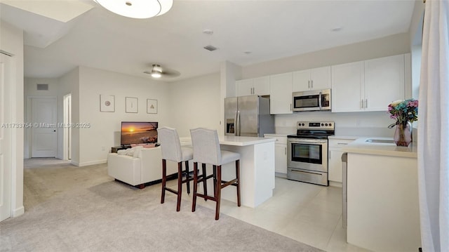 kitchen featuring appliances with stainless steel finishes, white cabinetry, a breakfast bar area, a center island, and light colored carpet