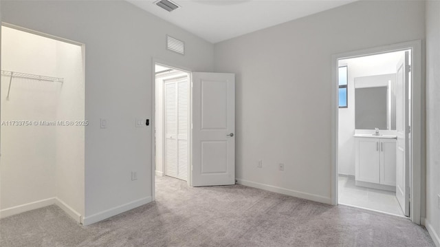 unfurnished bedroom featuring connected bathroom, sink, a spacious closet, a closet, and light colored carpet