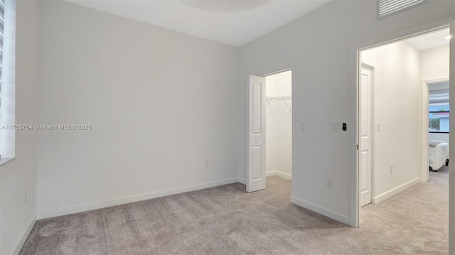 unfurnished bedroom with light carpet, a spacious closet, and a closet