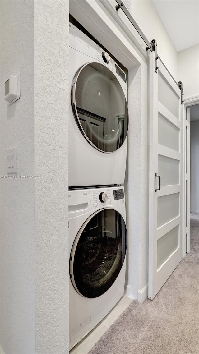 clothes washing area featuring stacked washer and dryer, a barn door, and light carpet