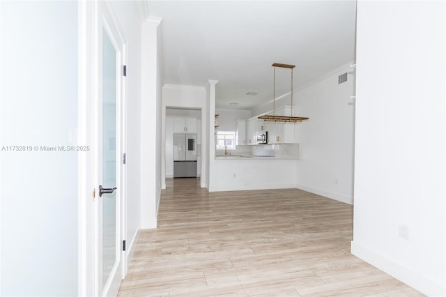 unfurnished living room with a sink, visible vents, baseboards, light wood-type flooring, and crown molding