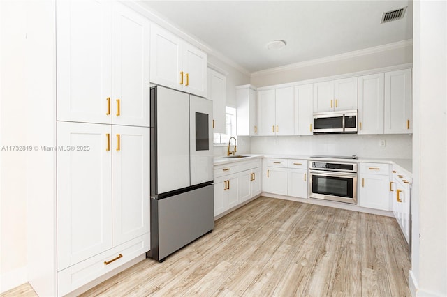 kitchen with light countertops, appliances with stainless steel finishes, ornamental molding, white cabinetry, and a sink