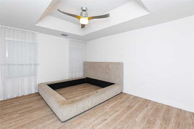 unfurnished bedroom with wood finished floors, visible vents, baseboards, a ceiling fan, and a raised ceiling