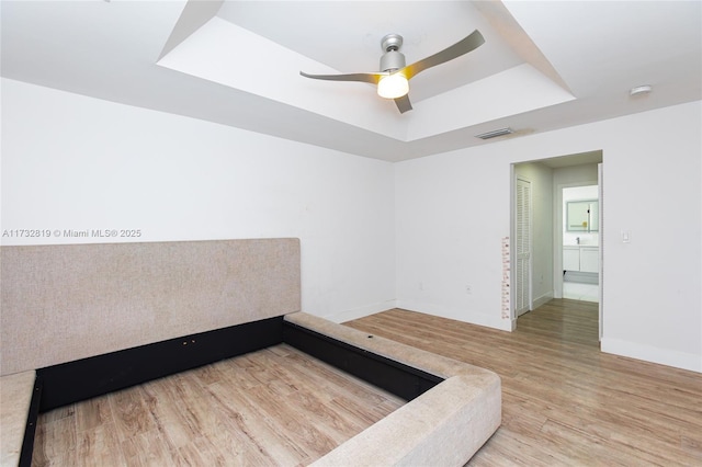 unfurnished room with baseboards, visible vents, a raised ceiling, ceiling fan, and light wood-style floors