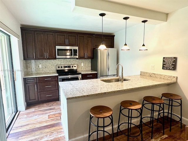 kitchen featuring sink, backsplash, light stone counters, kitchen peninsula, and stainless steel appliances