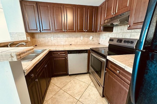 kitchen featuring light tile patterned flooring, appliances with stainless steel finishes, tile countertops, sink, and decorative backsplash