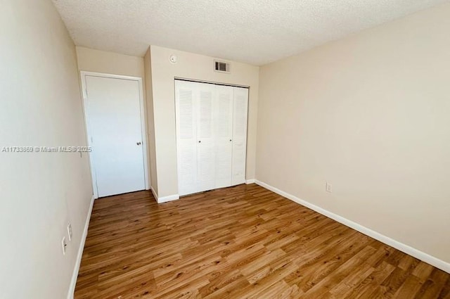 unfurnished bedroom with hardwood / wood-style floors, a closet, and a textured ceiling