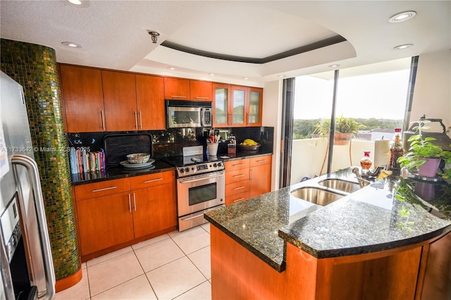 kitchen featuring sink, a center island with sink, light tile patterned floors, appliances with stainless steel finishes, and a tray ceiling