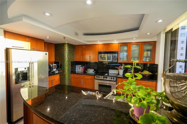 kitchen with dark stone countertops, backsplash, a raised ceiling, and appliances with stainless steel finishes