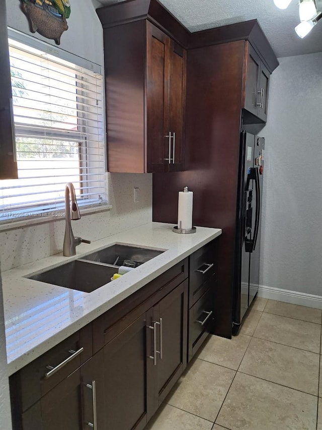 kitchen with light tile patterned flooring, sink, light stone counters, and black refrigerator with ice dispenser