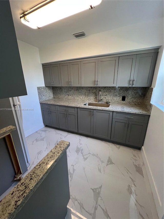 kitchen with tasteful backsplash, sink, light stone counters, and gray cabinets