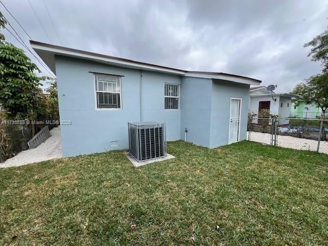 rear view of property with central AC unit and a lawn