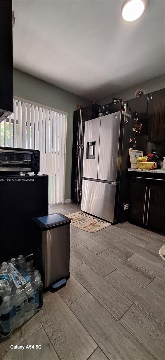 kitchen with dark brown cabinetry, stainless steel fridge, and light hardwood / wood-style floors