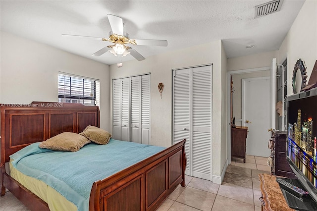 bedroom with light tile patterned floors, a ceiling fan, visible vents, and two closets