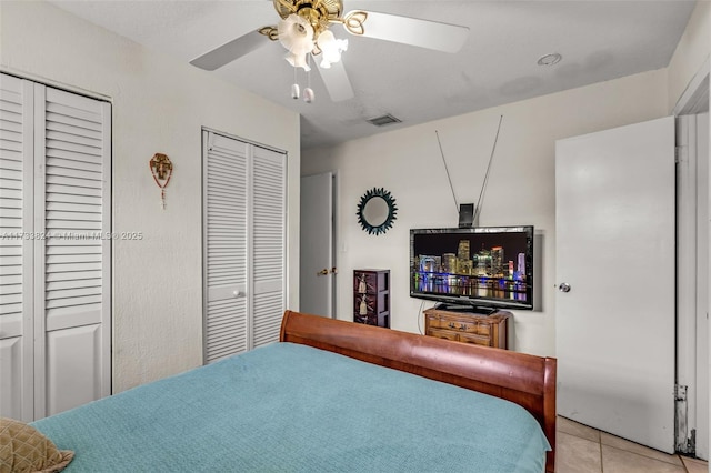 bedroom featuring light tile patterned floors, visible vents, ceiling fan, and two closets