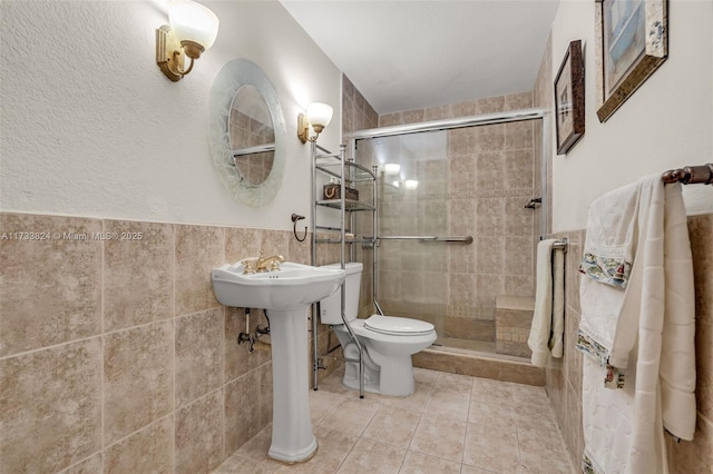 bathroom featuring a stall shower, wainscoting, toilet, tile patterned flooring, and tile walls