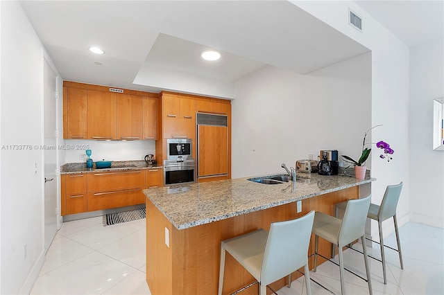 kitchen featuring stone counters, sink, a kitchen bar, kitchen peninsula, and paneled refrigerator