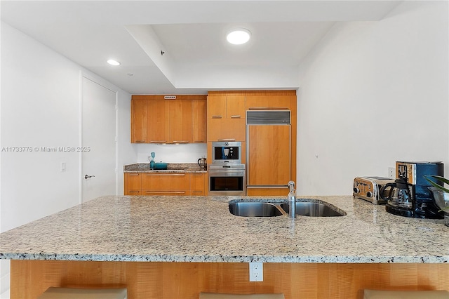 kitchen featuring paneled fridge, sink, kitchen peninsula, light stone countertops, and stainless steel double oven