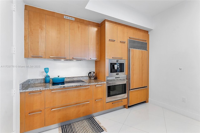 kitchen with dark stone countertops, paneled refrigerator, light tile patterned floors, and black electric stovetop