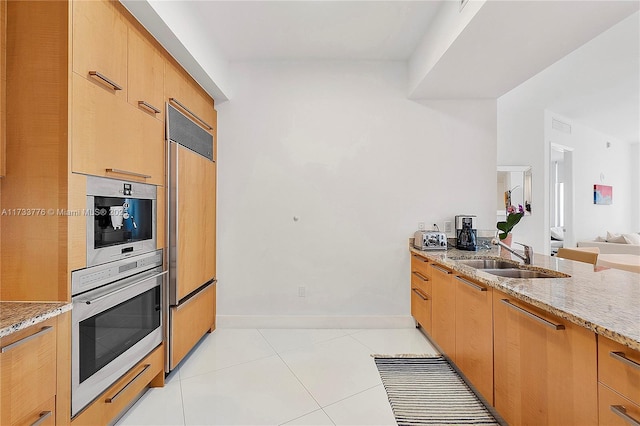 kitchen featuring light tile patterned flooring, sink, oven, paneled built in refrigerator, and light stone counters