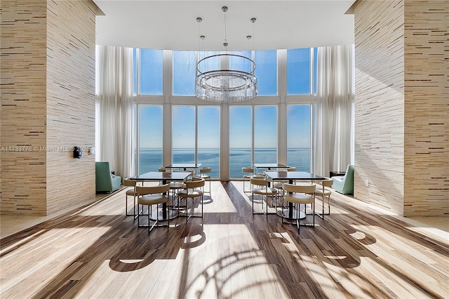 dining space with an inviting chandelier, a towering ceiling, wood-type flooring, and a water view