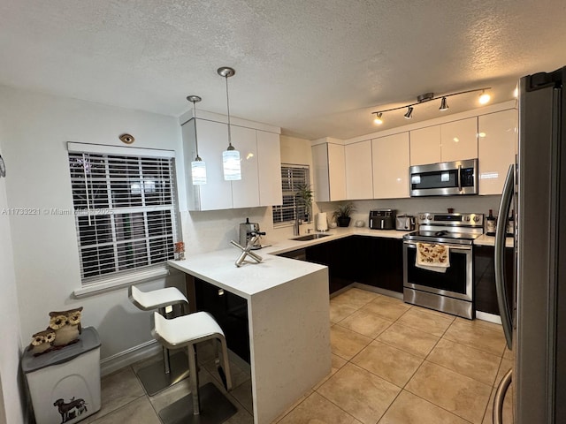 kitchen with appliances with stainless steel finishes, decorative light fixtures, white cabinetry, kitchen peninsula, and a textured ceiling