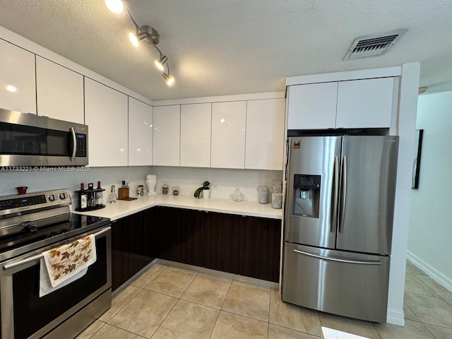 kitchen featuring appliances with stainless steel finishes, white cabinets, light tile patterned floors, dark brown cabinets, and a textured ceiling