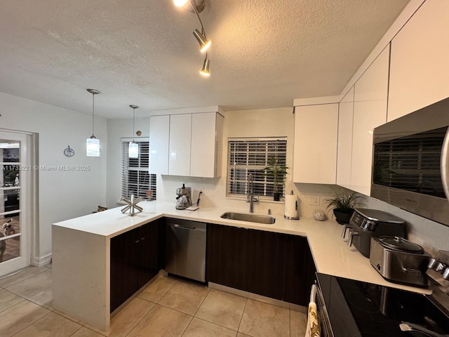 kitchen featuring sink, appliances with stainless steel finishes, white cabinetry, light tile patterned flooring, and decorative light fixtures