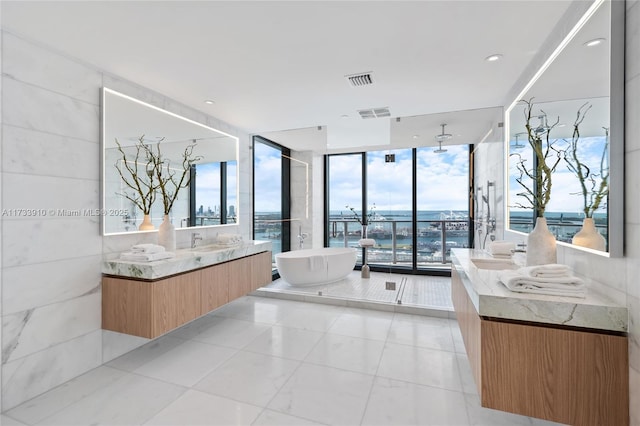 full bathroom featuring two vanities, visible vents, a freestanding bath, expansive windows, and a sink