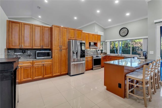 kitchen with a breakfast bar, tasteful backsplash, vaulted ceiling, appliances with stainless steel finishes, and wall chimney range hood